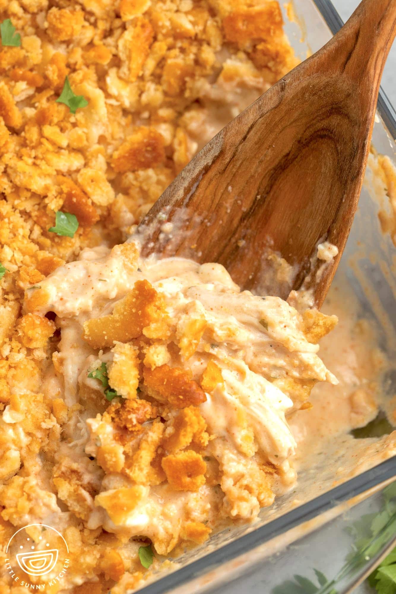 Close-up of an easy dinner idea: a casserole dish with creamy chicken mixture topped with crumbled golden brown biscuits, garnished with green onions, and a wooden spoon scooping out a serving