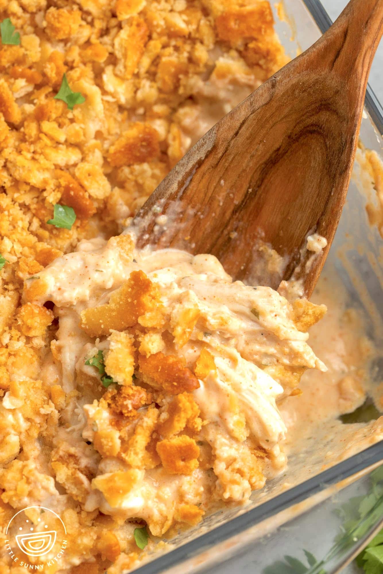 Close-up of an easy dinner idea: a casserole dish with creamy chicken mixture topped with crumbled golden brown biscuits, garnished with green onions, and a wooden spoon scooping out a serving