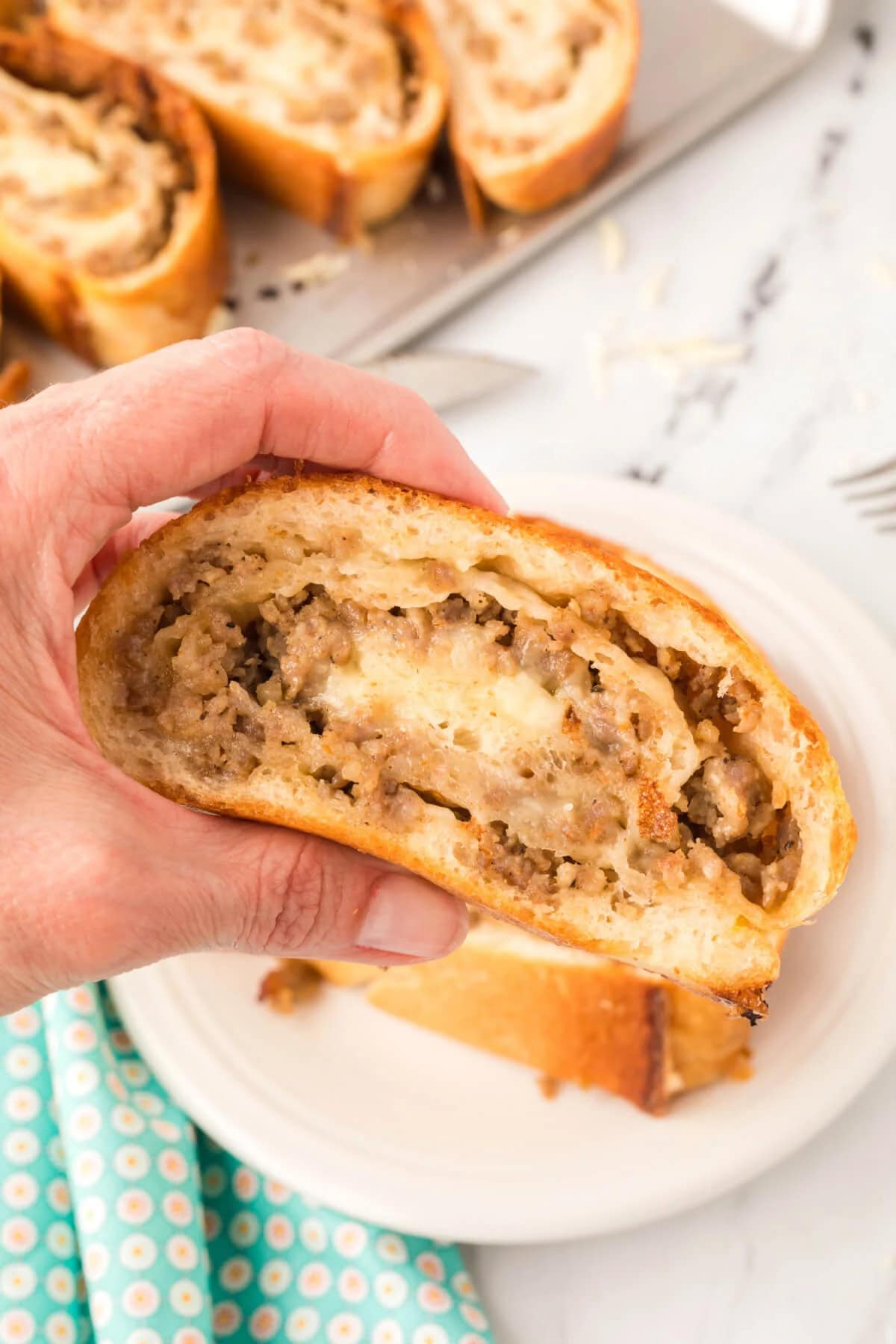 A close-up of a hand holding a slice of homemade sausage bread, revealing its savory minced meat and onion filling encased in a golden-brown crust, offering an easy dinner idea for busy families.