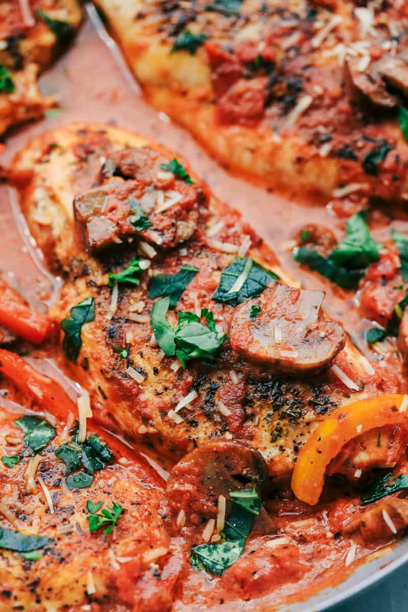Close-up view of a dish featuring chicken breasts cooked in tomato sauce, garnished with sliced sausage, bell peppers, and chopped herbs—perfect for busy families seeking easy dinner ideas.