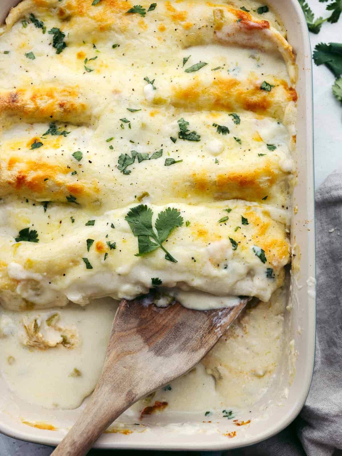 A baked white sauce and cheese lasagna in a white dish, topped with golden-brown spots and garnished with chopped parsley, serving as an easy dinner idea for busy families, with a wooden spoon