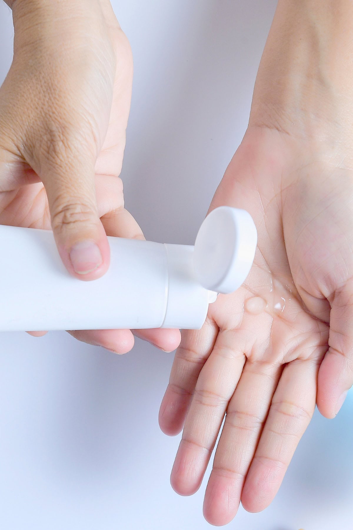 Two hands are in the image: one holding a white tube and squeezing homemade diy hair gel onto the open palm of the other hand. The hair gel being dispensed suggests the use of an organic, safe skincare or hygiene product. The background is plain white.
