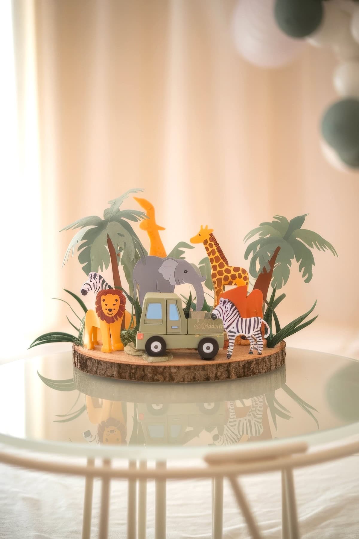 A baby shower centerpiece showcases paper cutouts of safari animals, like a zebra, lion, giraffe, and elephant, nestled among palm trees and a toy jeep on a wooden base atop a glass table.