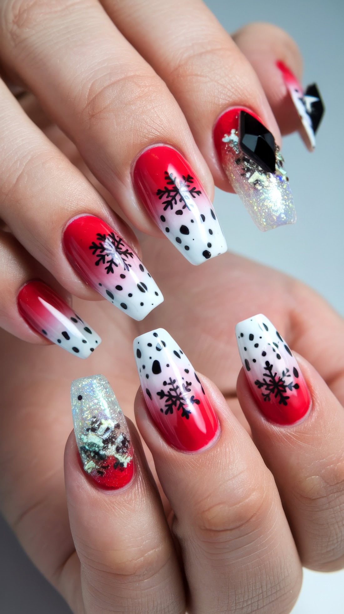 Close-up of a hand with red and white Disney Christmas nails, featuring black snowflakes and dots giving the idea of 101 Dalmation or Cruella de Vil designs. Some nails include glittery accents and playful black geometric shapes, crafting a festive and bold winter-themed design.
