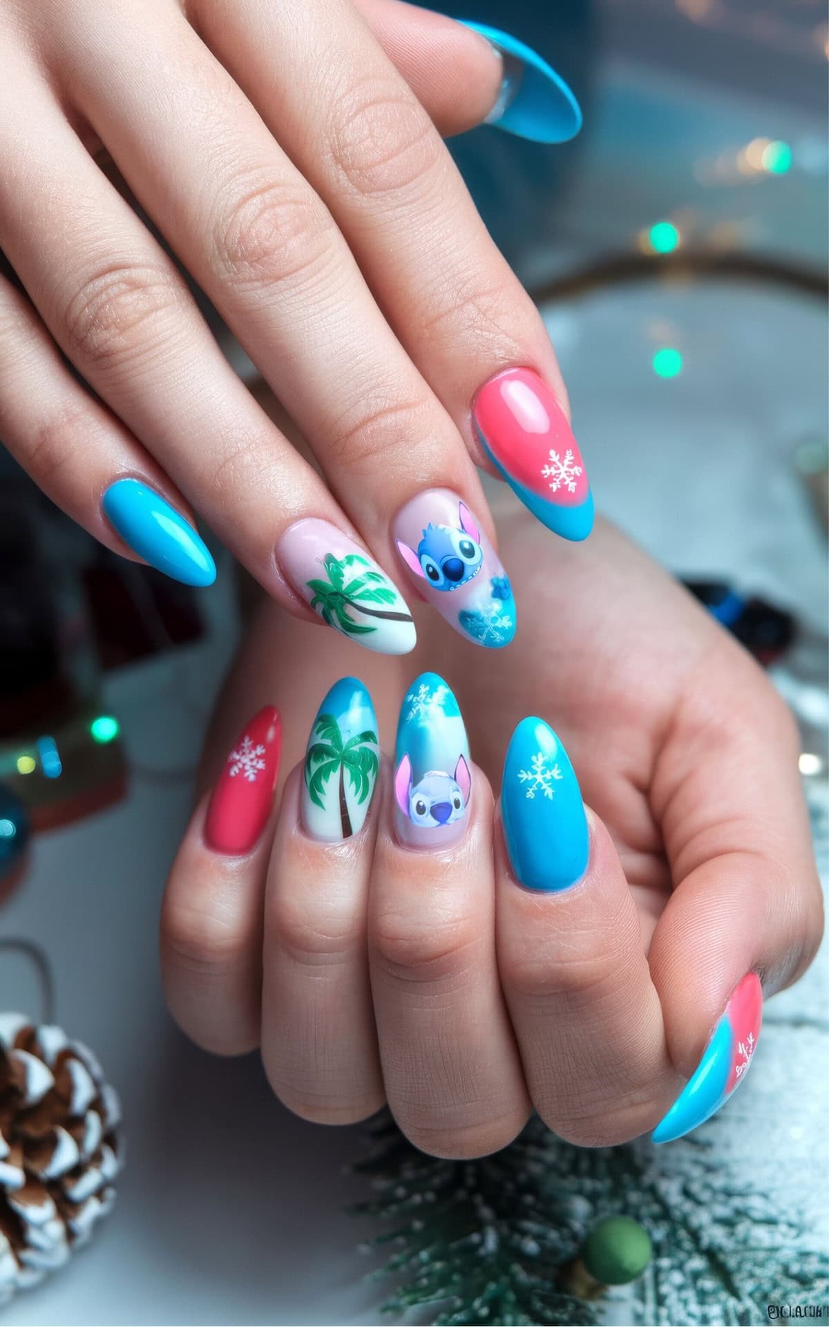 Close-up of manicured hands with colorful Disney Christmas nail art. Nail design is a Lilo and Stitch theme, and includes snowflakes, palm trees, and the Stitch character on a mix of aqua, pink, and white backgrounds. A holiday-themed setting with pine cones and decorative lights is visible.