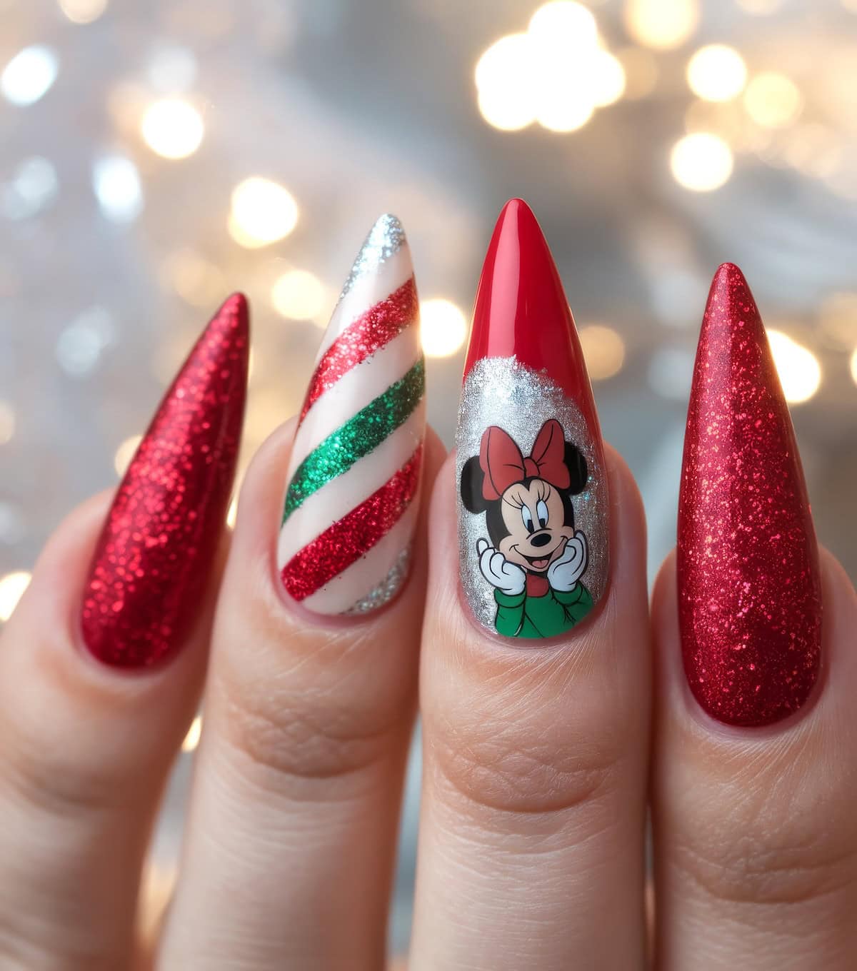 Close-up of festive Disney Christmas nails on four fingers of one hand. They boast sparkly red polish, one with silver glitter, red and green stripes, and another showcasing Minnie Mouse in a green outfit. The blurred lights in the background enhance the holiday vibe.