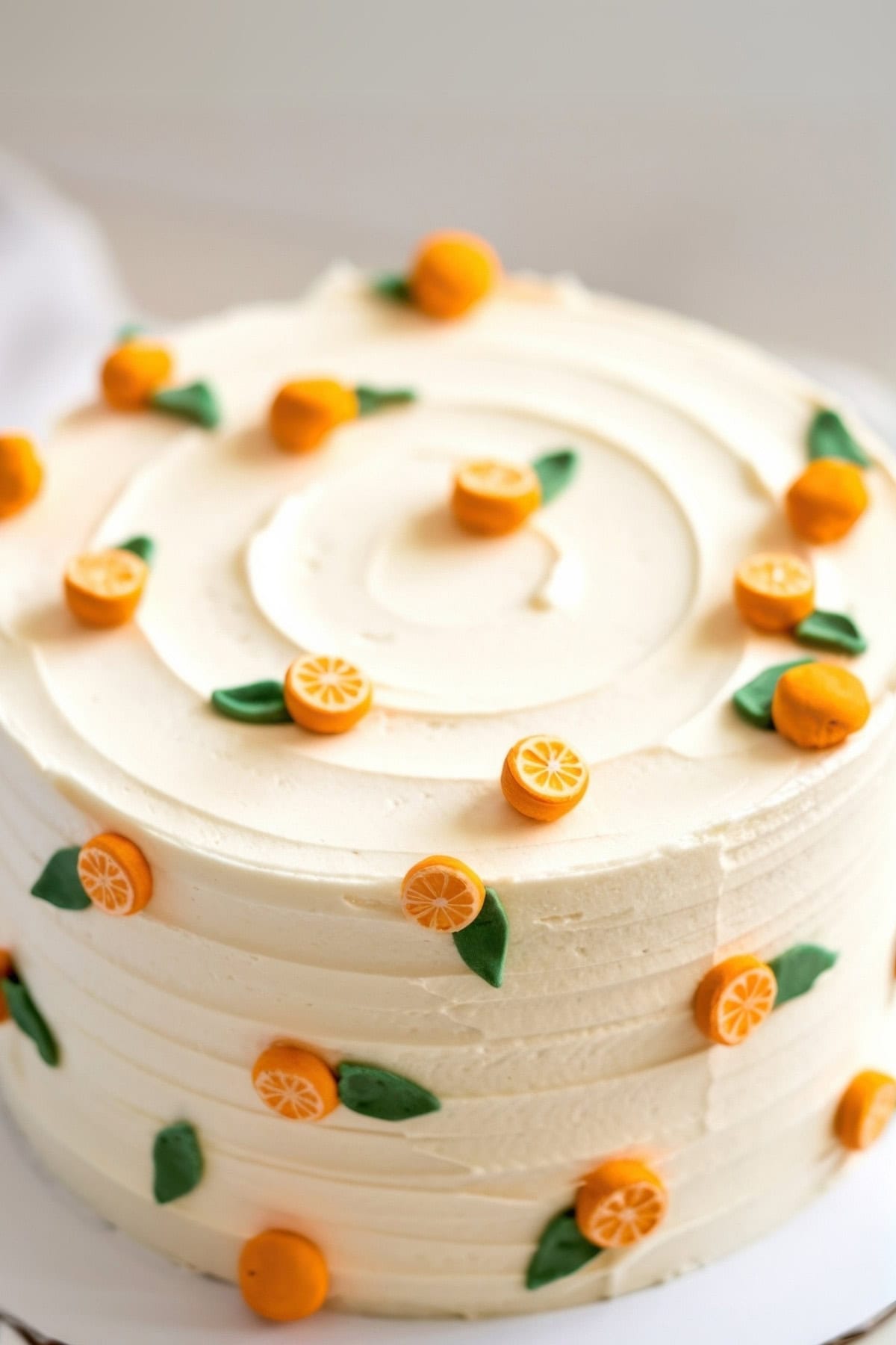 A frosted cake is a centerpiece among little cutie baby shower ideas, decorated with small orange fondant fruits and lush green leaves. The halved fruits reveal detailed interiors and top a beautifully smooth, spiral frosting pattern.