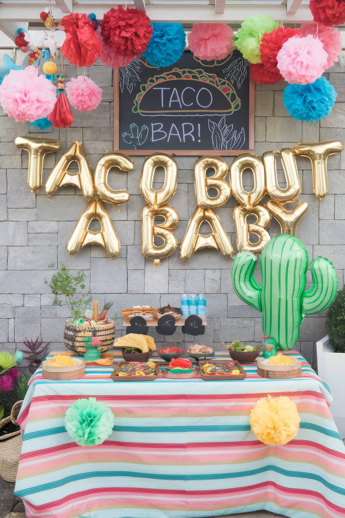 Colorful taco-themed baby shower setup, perfect for summer baby shower ideas, featuring "TACO 'BOUT A BABY" gold balloons, a taco bar sign, festive paper decorations, a cactus prop, and a table with vibrant taco ingredients and dishes.