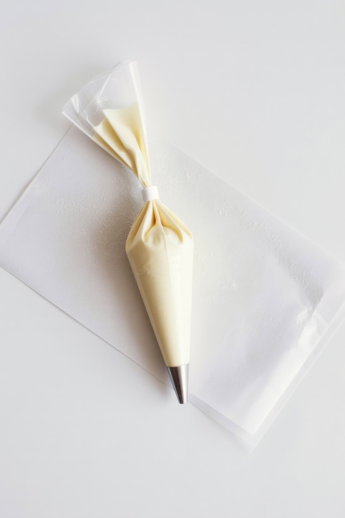 A piping bag filled with melted white chocolate, fitted with a metal tip, rests on a sheet of parchment paper—perfect for decorating Oreo Balls or adding flair to Patriotic Desserts against a white background.
