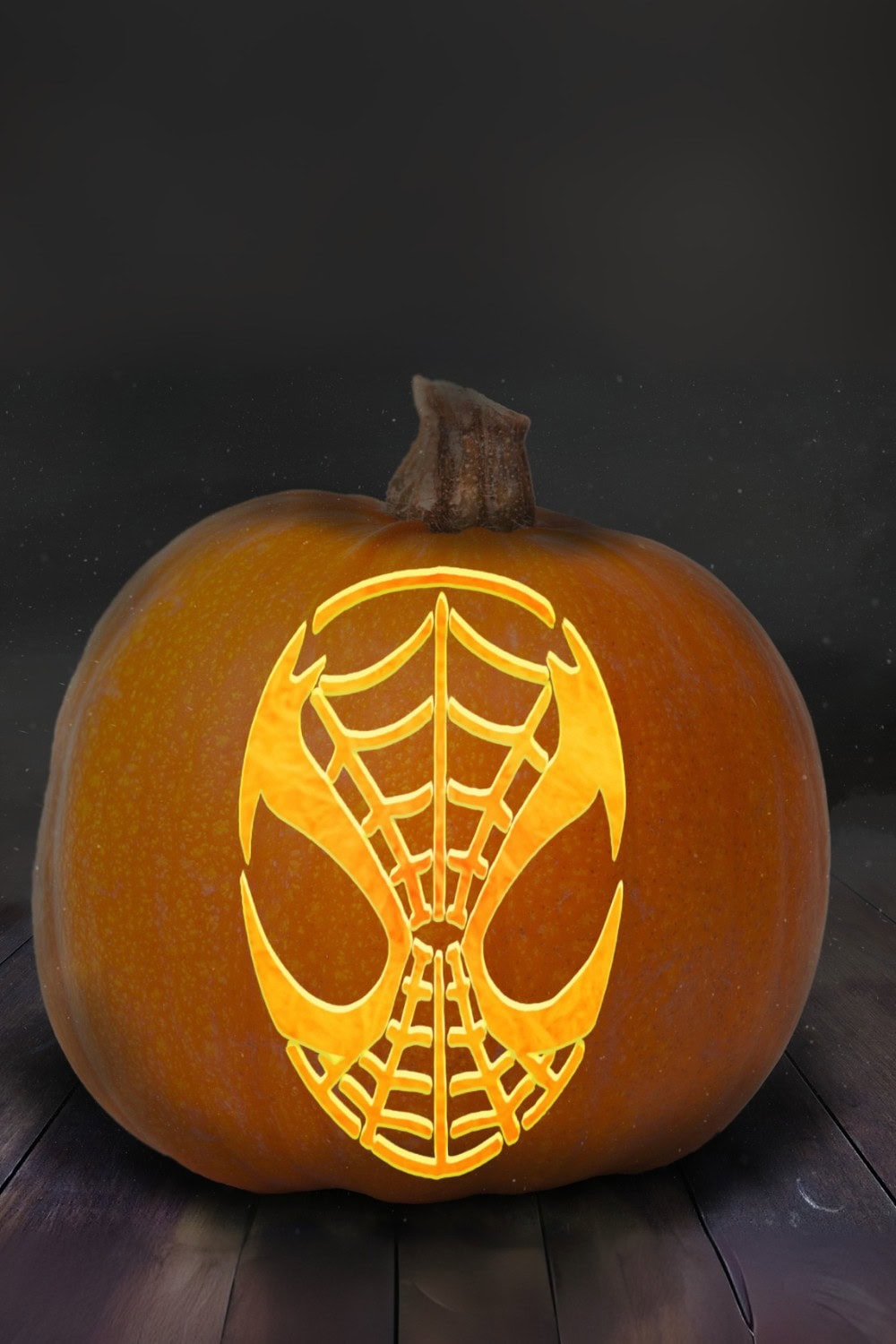 A pumpkin is carved with a Spider-Man mask design using Spiderman Pumpkin Stencils, featuring web patterns and large eyes, and is illuminated from within, glowing against a dark background.